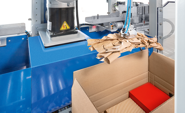 Ein Papierpolster wird vollautomatisch in einen Karton mit Versandgütern gelegt.