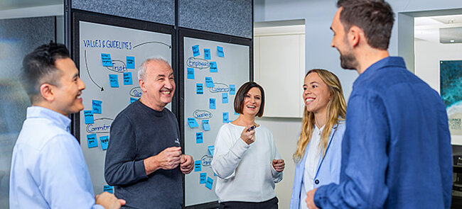 
			Colleagues standing together in the office during a meeting