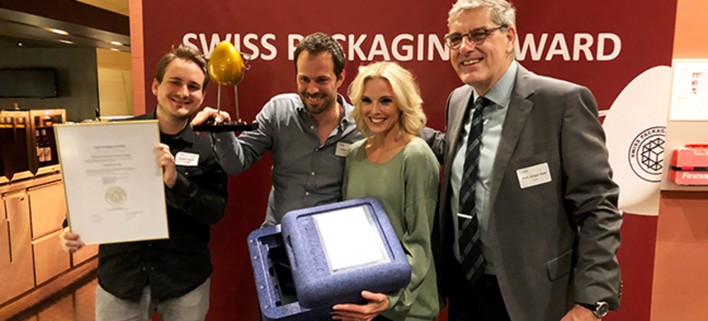 Vier Personen sind zusammen mit einer Urkunde und einer Verpackungsbox auf einem Bild.